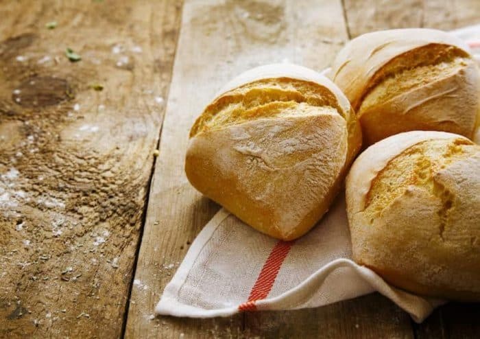 Crisp freshly baked crusty rolls on a napkin on old rustic wooden boards