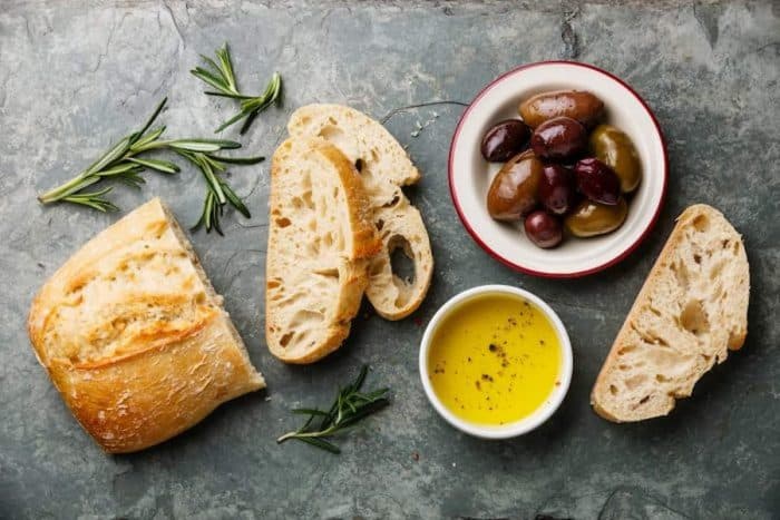 Sliced fresh bread Ciabatta with olive oil, olives and rosemary on gray stone slate background