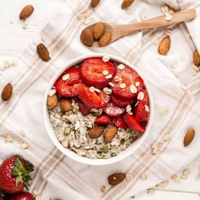 a bowl of chia seeds, oats, pumpkin seeds, sunflower seeds, almonds, and milk topped with fresh fruits