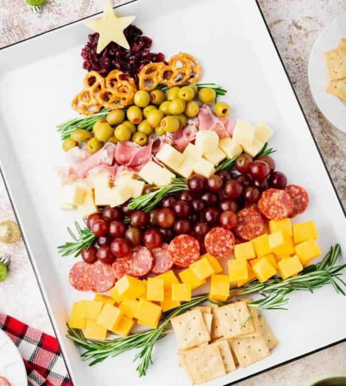 This edible Christmas tree is made with cheese cubes, olives, grapes, salami, prosciutto, raisins, pretzels, crackers, rosemary sprigs, and a cheese-shaped star.