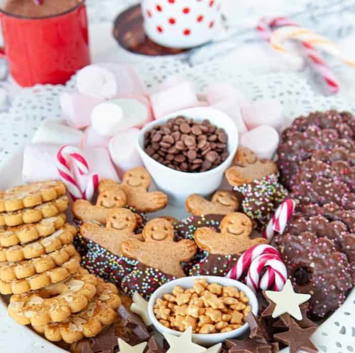 The embodiment of ultimate winter comfort, this hot chocolate charcuterie board overflows with marshmallows, cookies, gingerbread men, chocolates, candies, and candy canes.