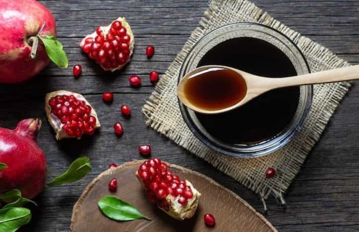 pomegranate sour sauce with fresh ripe whole and split pomegranate fruit on wooden rustic table