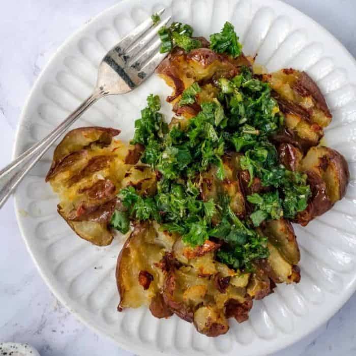 boil baby potatoes until tender, flatten them gently to create craggy surfaces, then roast them with olive oil and top afterward with an herb and garlic chimichurri
