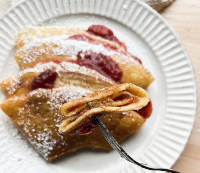 These delectable sourdough discard crepes offer a delightful way to repurpose excess sourdough discard, a woman holding a spoonful of crepe