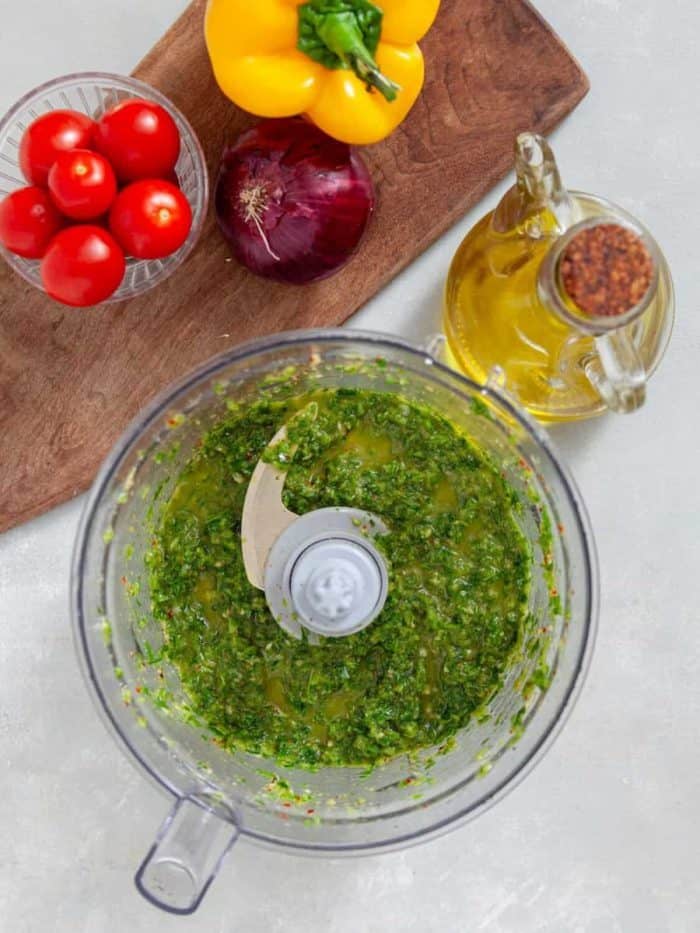 In a food processor, blend cilantro, parsley, jalapeño peppers, garlic, salt, cumin, and chili flakes, then drizzle in olive oil until the mixture reaches a saucy consistency.