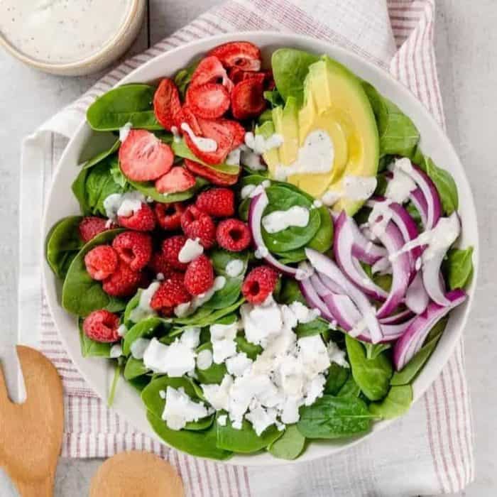 Delicate spinach leaves create a bed for the vibrant elements in this salad, including raspberries, avocado, and strawberries.