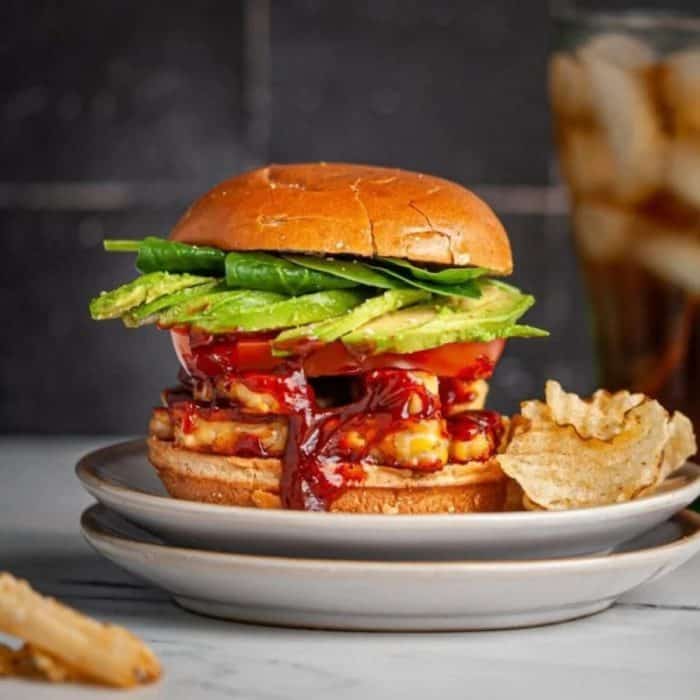 a photo of bbq tempeh burger sandwich with chips on the side on two layers of white round plate