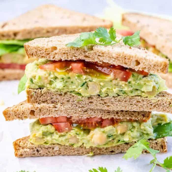 a close up photo of two layers of chickpea avocado sandwich on a white surface