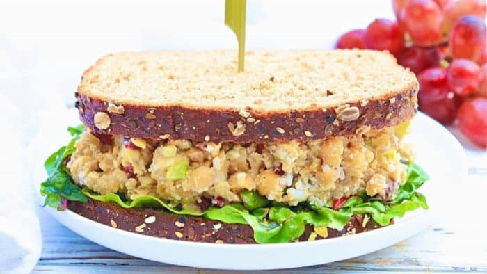 a photo of cranberry walnut chickpea salad sandwich on a white plate