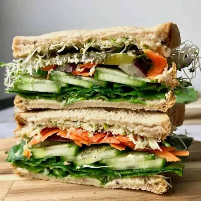 a photo of two layers cucumber hummus sandwich on a wooden chopping board