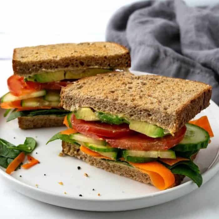 a photo of two pieces of cucumber hummus vegan sandwich on a round white plate