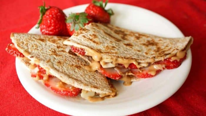 a photo of peanut butter torilla sandwich on a white plate on a red table