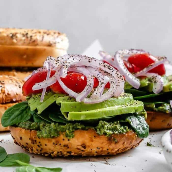 a photo of pesto bagels plant based vegan sandwich topped with lots of onions
