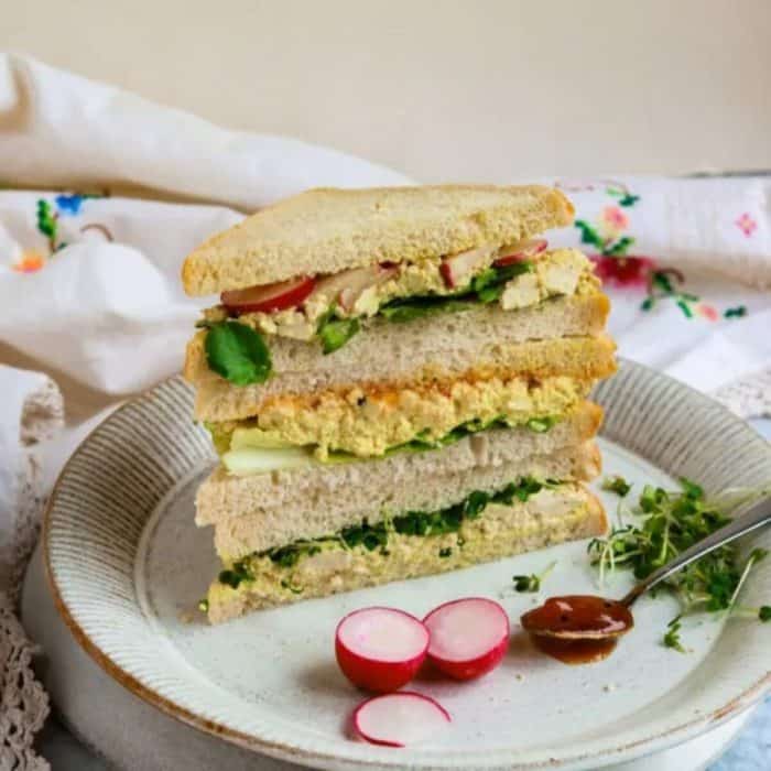 a photo of tofu egg salad vegan sandwich layered on a white round plate