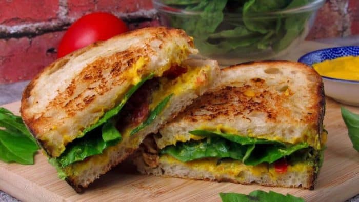 two slices of pesto grilled cheese vegan sandwich on top of a wooden chopping board