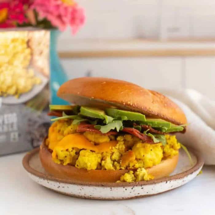 a photo of vegan breakfast burger sandwich with avocado on top of a small round plate