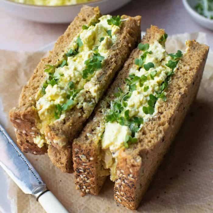 a photo of vegan egg mayo sandwich on top of a brown tissue an a knife beside it