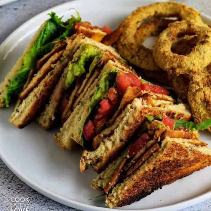 a photo of a blt tofu sandwich and onion rings on a round white plate