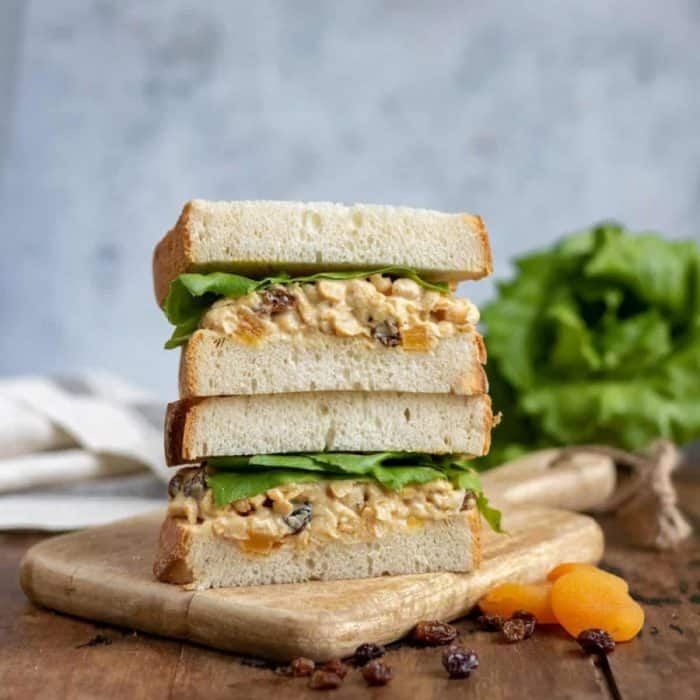 two layers of slices of coronation chickpea vegan sandwich on a wooden chopping board