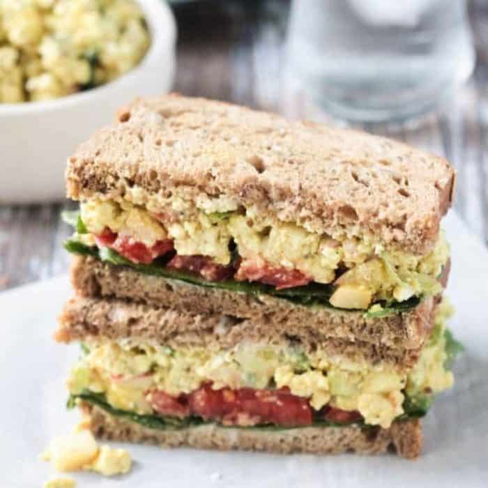 a close up photo of two layers of curried tofu salad sandwich on a white plate