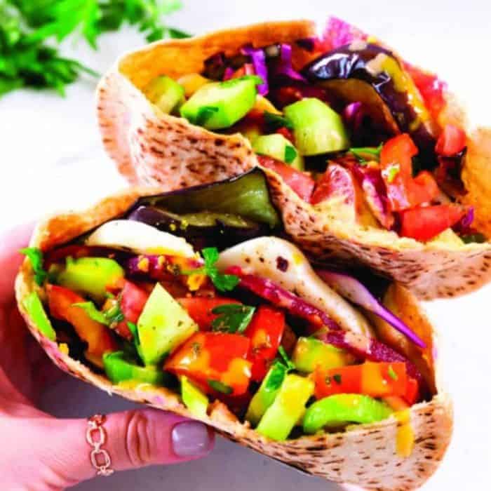 a woman's hand holding a sabich vegetarian pita sandwich