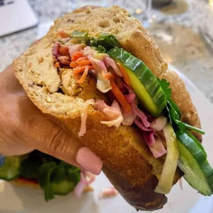 a close up photo of a hand holding a tofu banh mi vegan sandwich