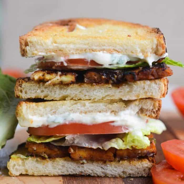 a close u photo of blt vegan sandwich on top of a wooden chopping board