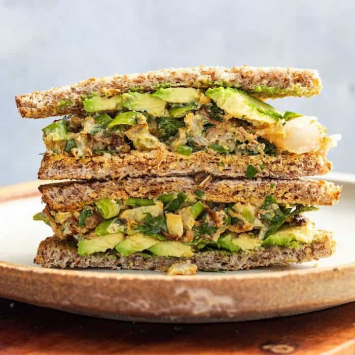 a photo of two layers of vegan sandwich with cauliflower salad spread standing on a wooden round plate