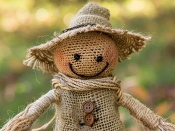 A burlap scarecrow doll with a straw hat and button eyes is smiling.