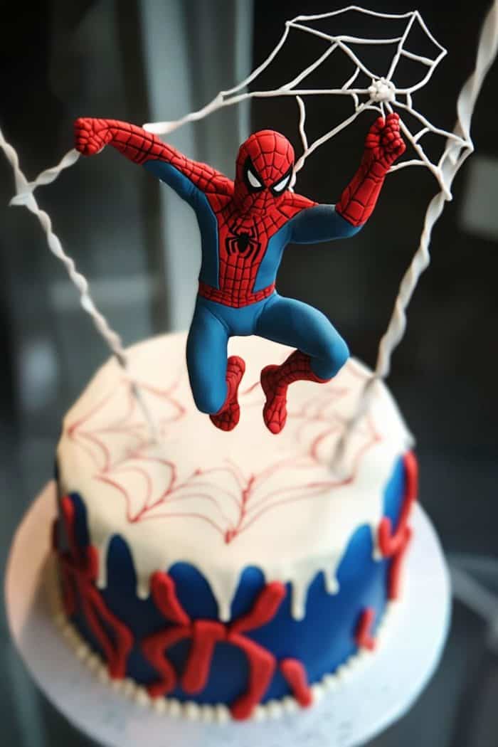 A cake decorated with a Spider-Man figure hanging from webs, with blue and red icing and spiderweb designs.