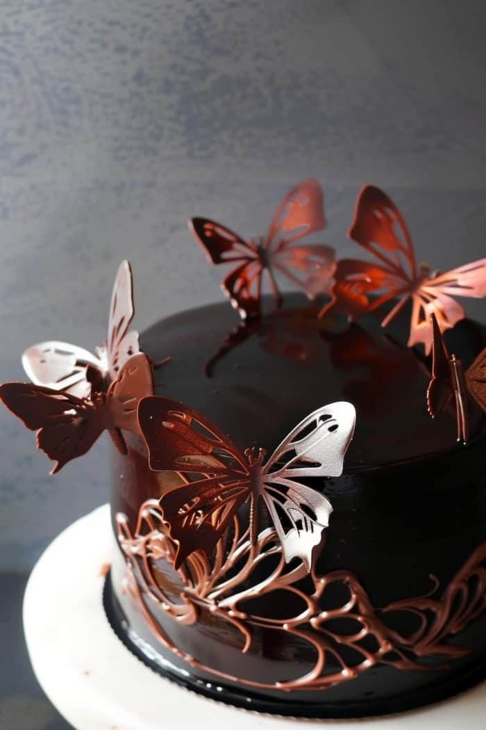Indulge in a luxurious treat by crafting delicate butterflies from tempered chocolate and placing them on a chocolate ganache-covered cake. 