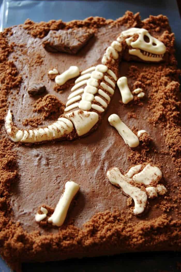 A chocolate cake decorated to resemble an excavation site, featuring edible dinosaur fossils and cookie crumbs as dirt.