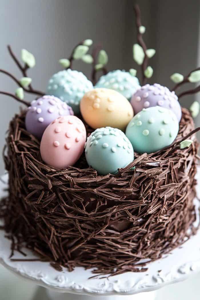 A cake designed to look like a dino egg nest, adorned with pastel-colored eggs and branches, on a white stand.