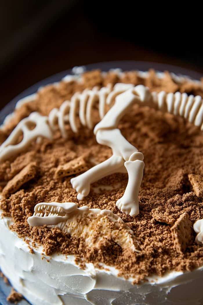 A cake decorated with a dinosaur fossil design, featuring bones and a layer of crumbled cookies resembling dirt.