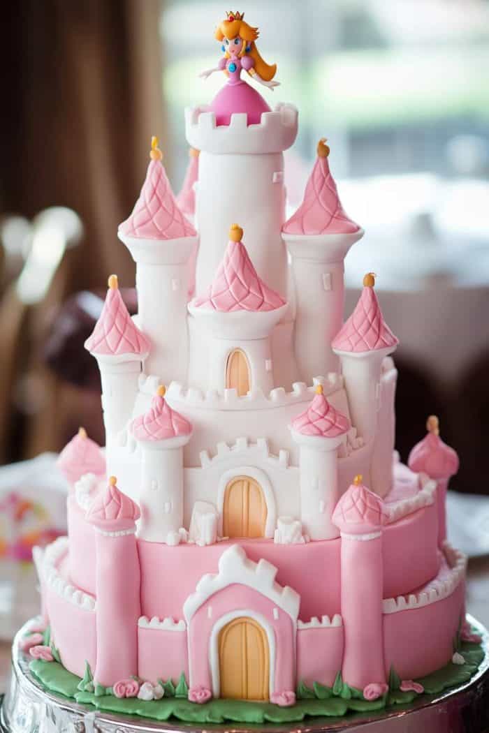 A multi-tiered cake designed as a pink and white castle with a princess figurine on the top tier, featuring detailed towers and arched doors.