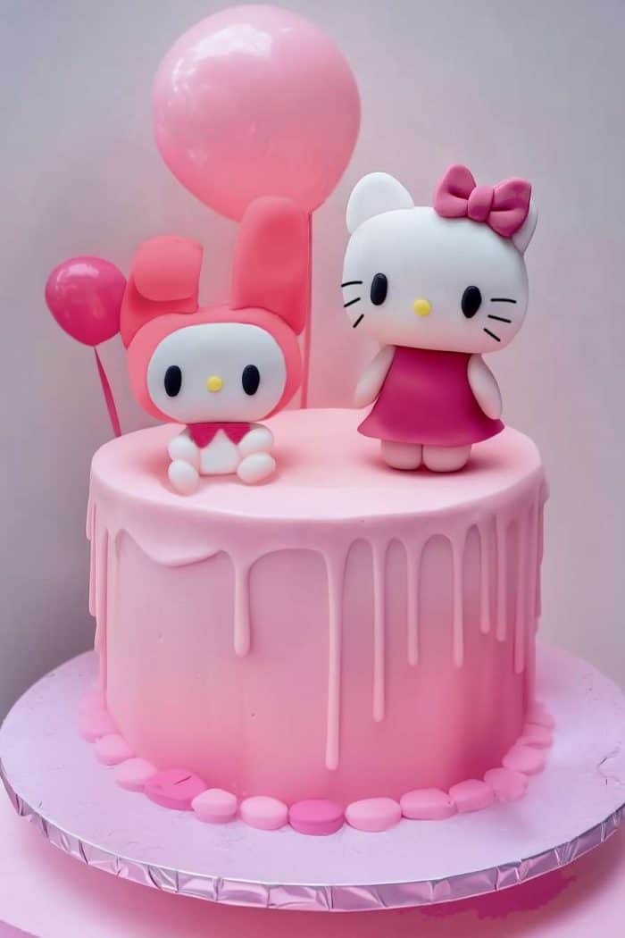 A pink, tiered cake with drip features two cartoon character toppers. One is Hello Kitty with a pink dress and bow; the other is Melody with pink ears. Pink balloons are in the background.