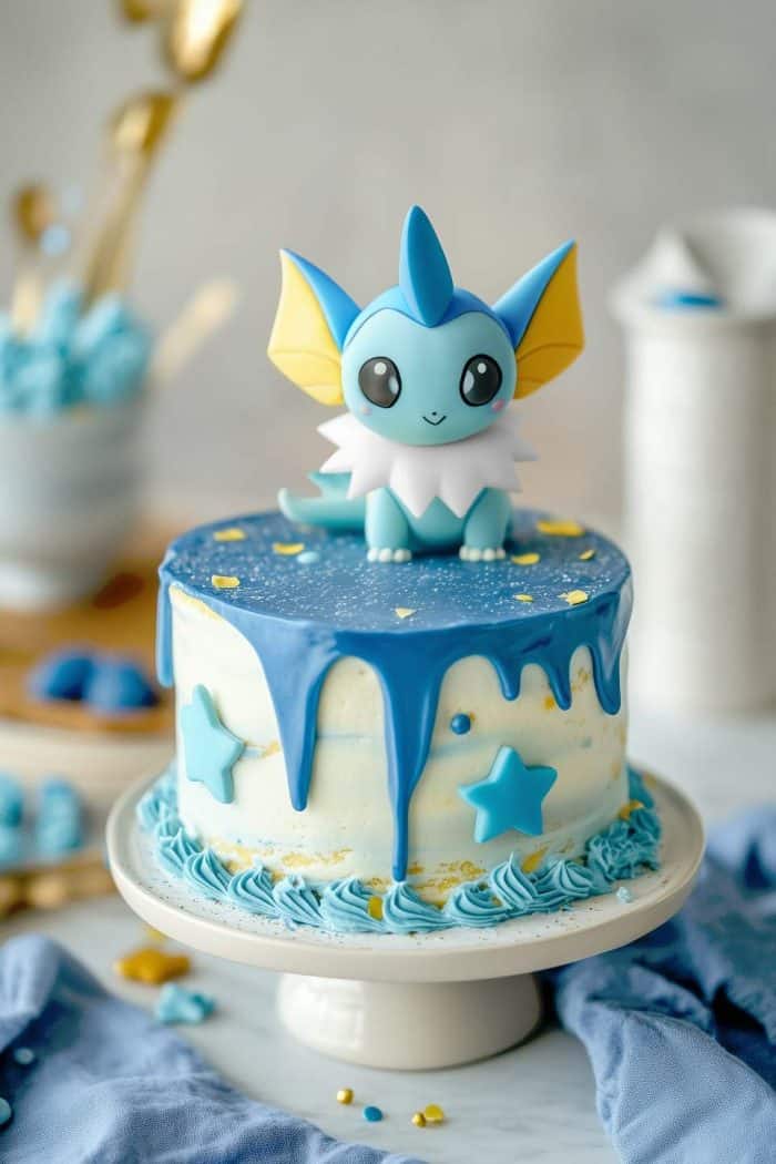 A cake with blue icing drips and star decorations is topped with a figurine of a blue, yellow, and white anime character. The cake sits on a white stand, with blue and gold accents visible in the background.