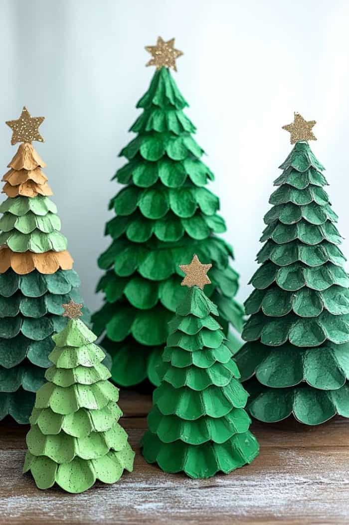 Handcrafted paper Christmas trees with layered green and gold textures and star toppers are displayed on a wooden surface.