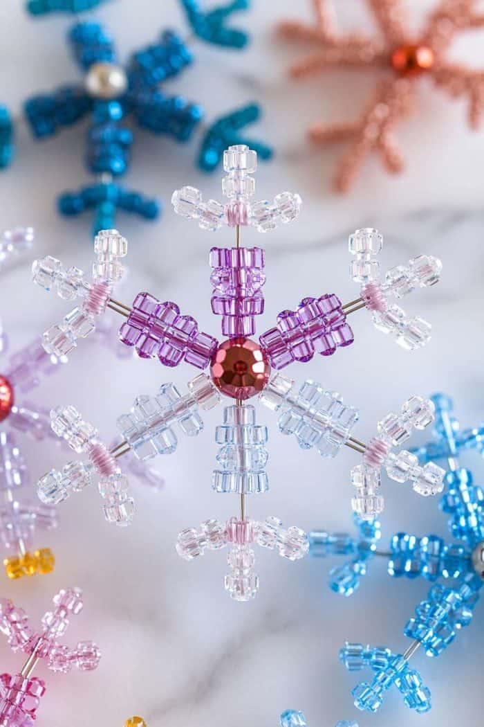 Assorted colorful bead snowflake ornaments on a marble surface.