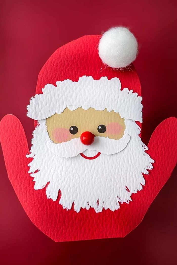 A paper craft depicting Santa Claus with a red hat and a white beard on a red background.