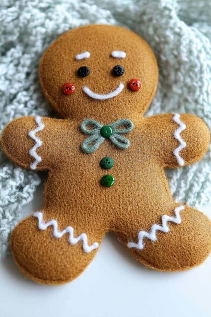 A felt gingerbread man plush with a green bow and button details, lying on textured fabric.