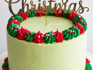 A festive Christmas cake with green frosting is topped with red and green decorative swirls and a "Merry Christmas" topper. The cake is displayed on a white plate with a simple design.