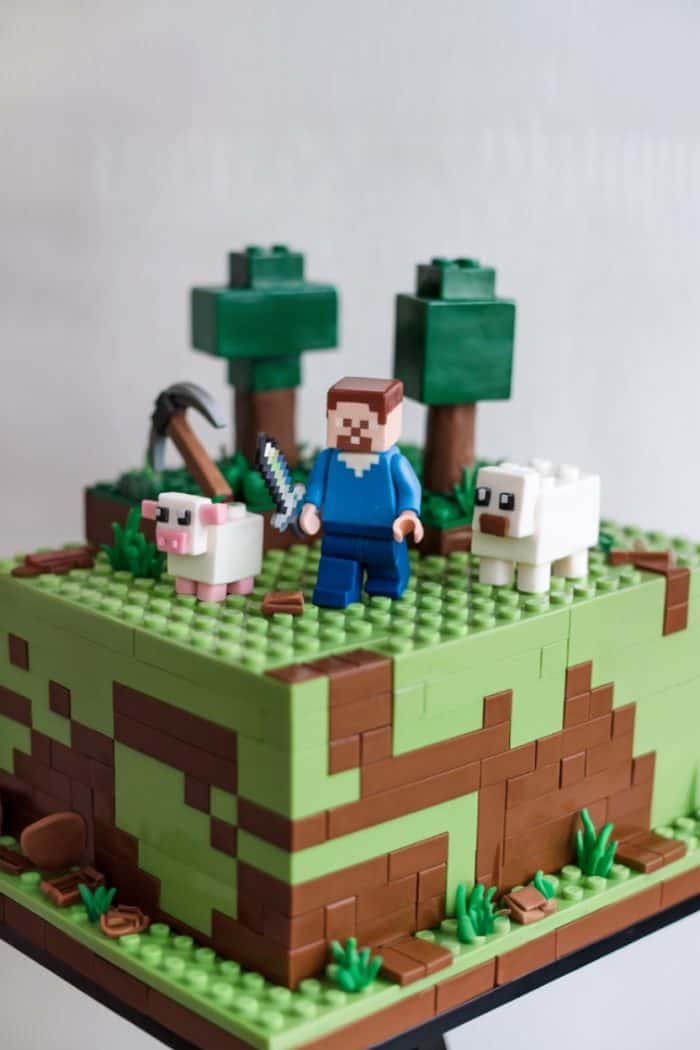 A blocky, pixelated landscape made of building bricks depicts a grassy terrain with trees. A character holding a sword stands beside a pig and a sheep, reminiscent of a popular video game design.