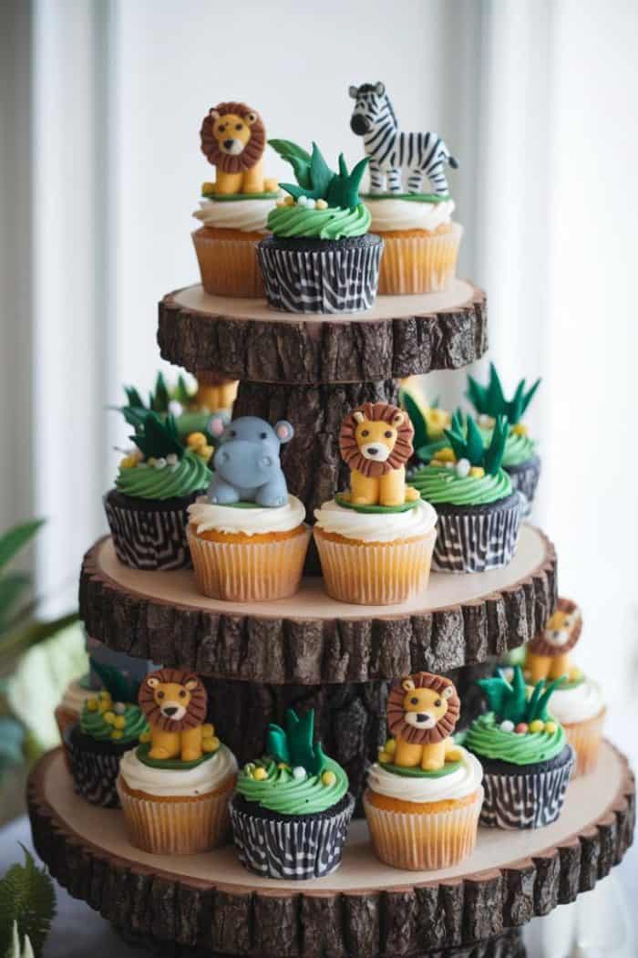A three-tiered cupcake stand made of wooden disks holds cupcakes decorated with jungle animal toppers, including lions, a zebra, and a hippo. The cupcakes also feature green frosting resembling grass and foliage.
