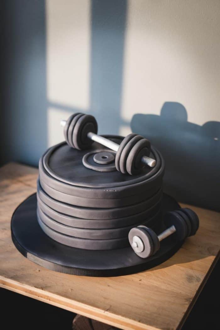 A cake designed to look like stacked weight plates with a barbell on a wooden table, bathed in sunlight.