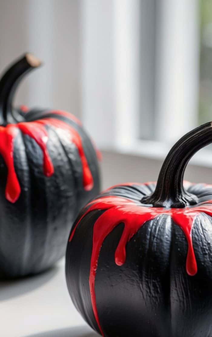 Two black pumpkins with red paint resembling dripping blood on top sit near a window, creating a dramatic and spooky atmosphere.