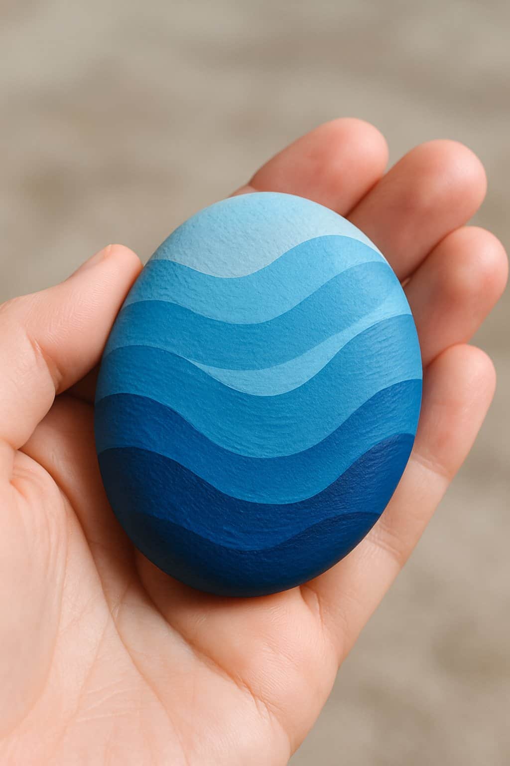 A hand holding a smooth river rock painted with blue designs.