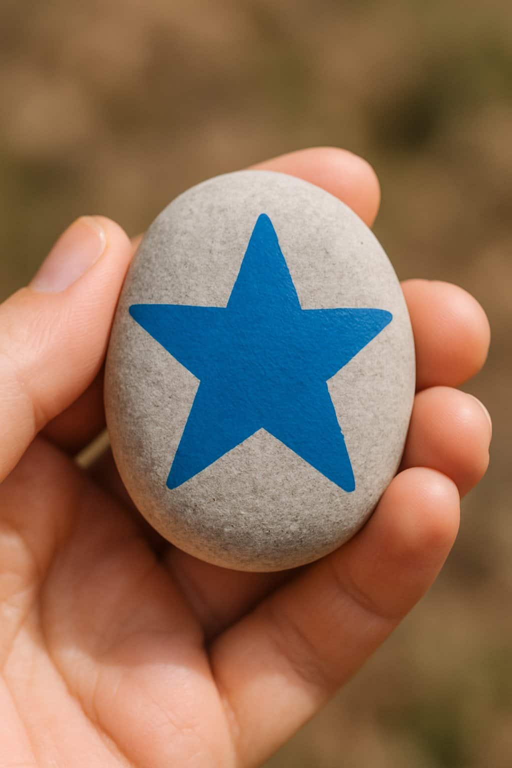 A hand holding a smooth river rock painted with a blue star pattern.
