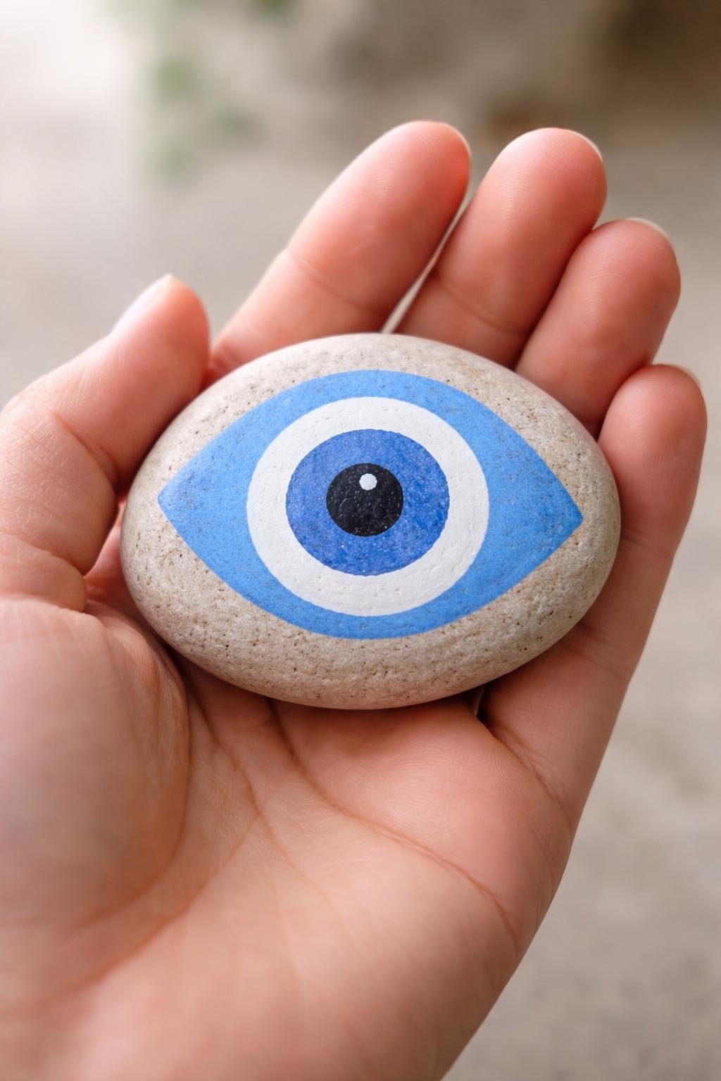 A hand holding a smooth river rock painted with a simple evil eye design.